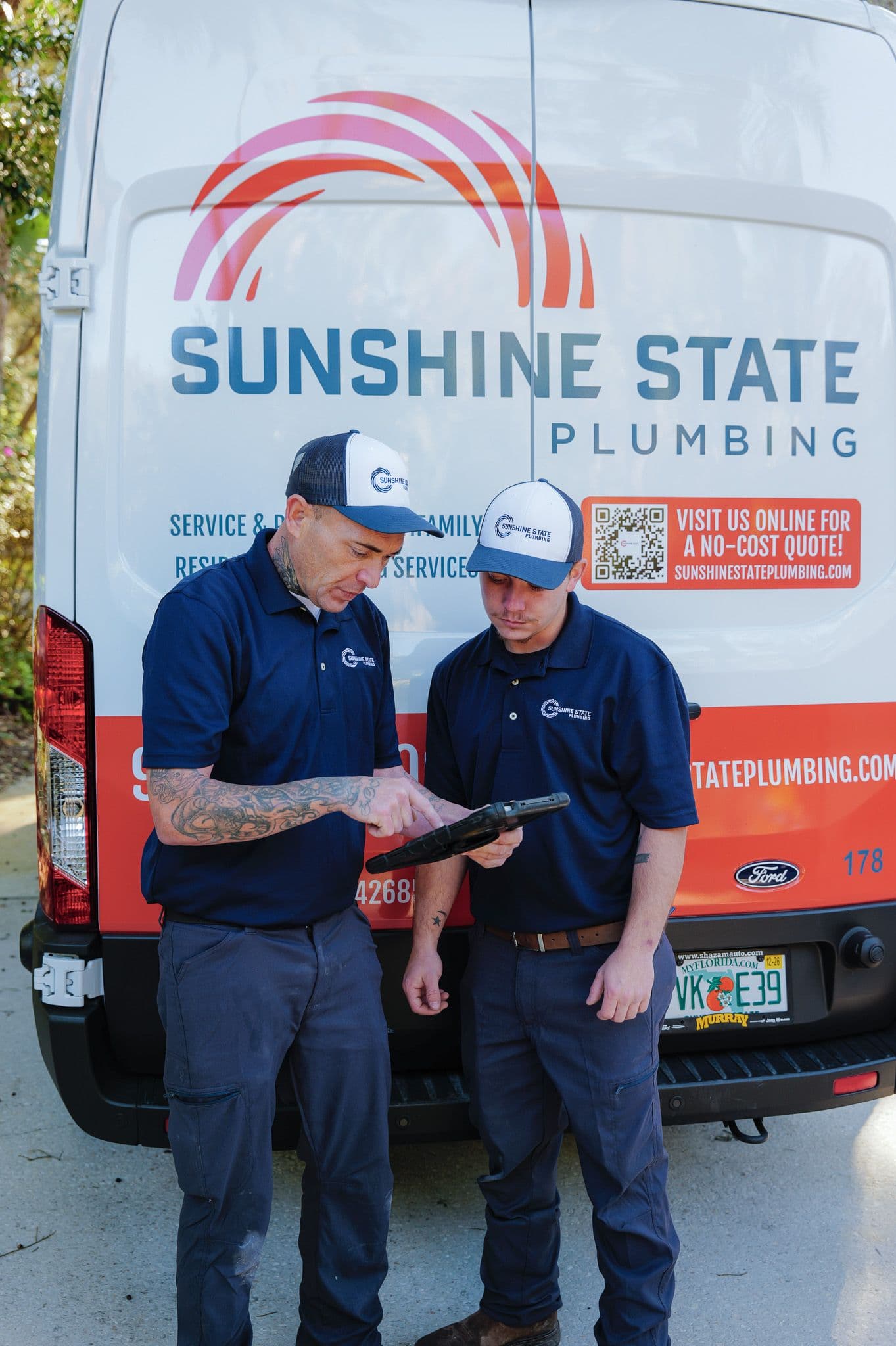 Two Sunshine State Plumbing technicians reviewing plans on a tablet at the work van