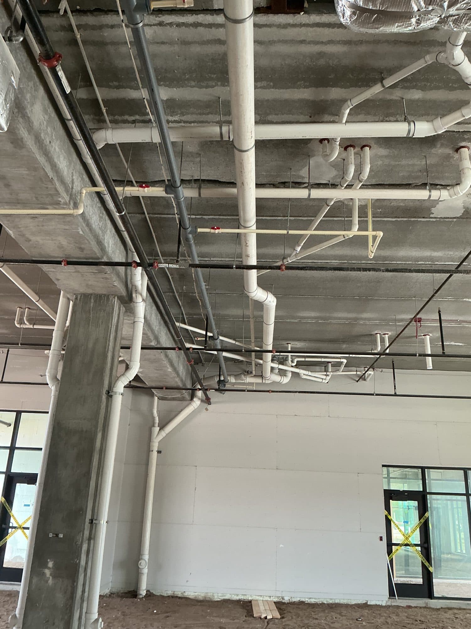 Overhead supply and waste piping roughed in across an open ceiling on a multifamily build